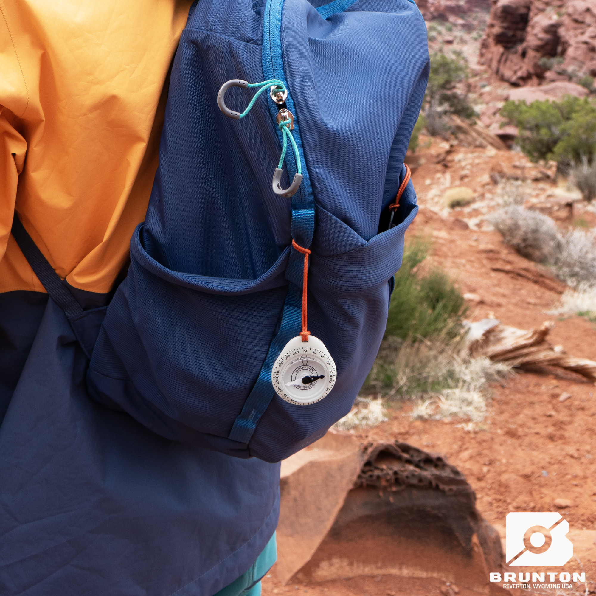 Person wearing a blue backpack with a compass attached, standing in a desert landscape.