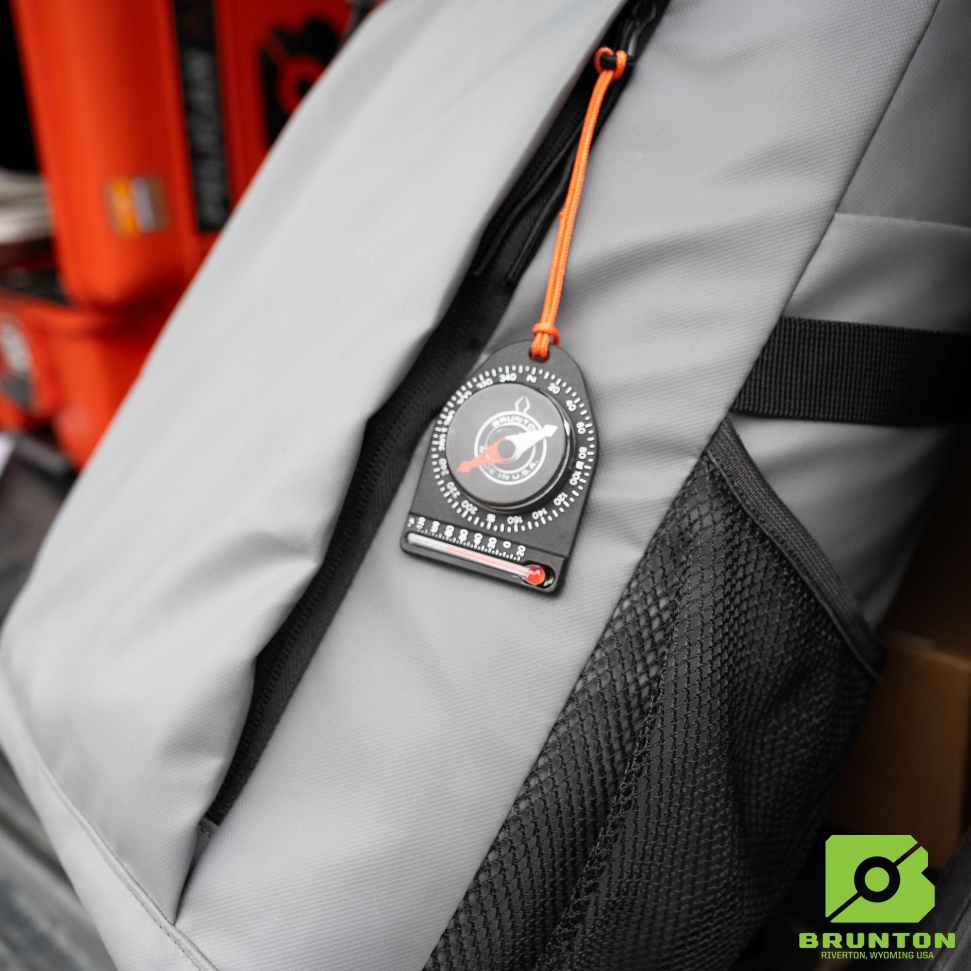 Brunton compass attached to a gray backpack.