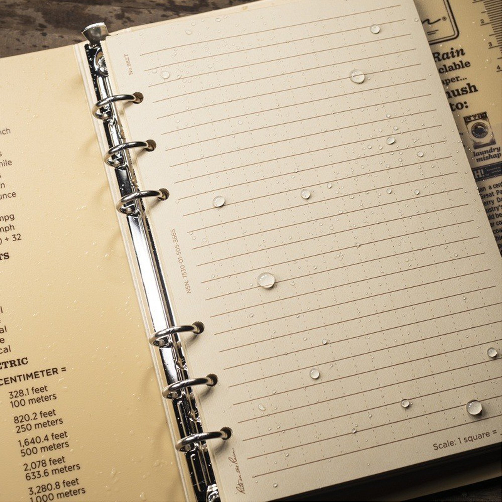 An tan ring binder with tan pages covered in water droplets on a dark textured surface.