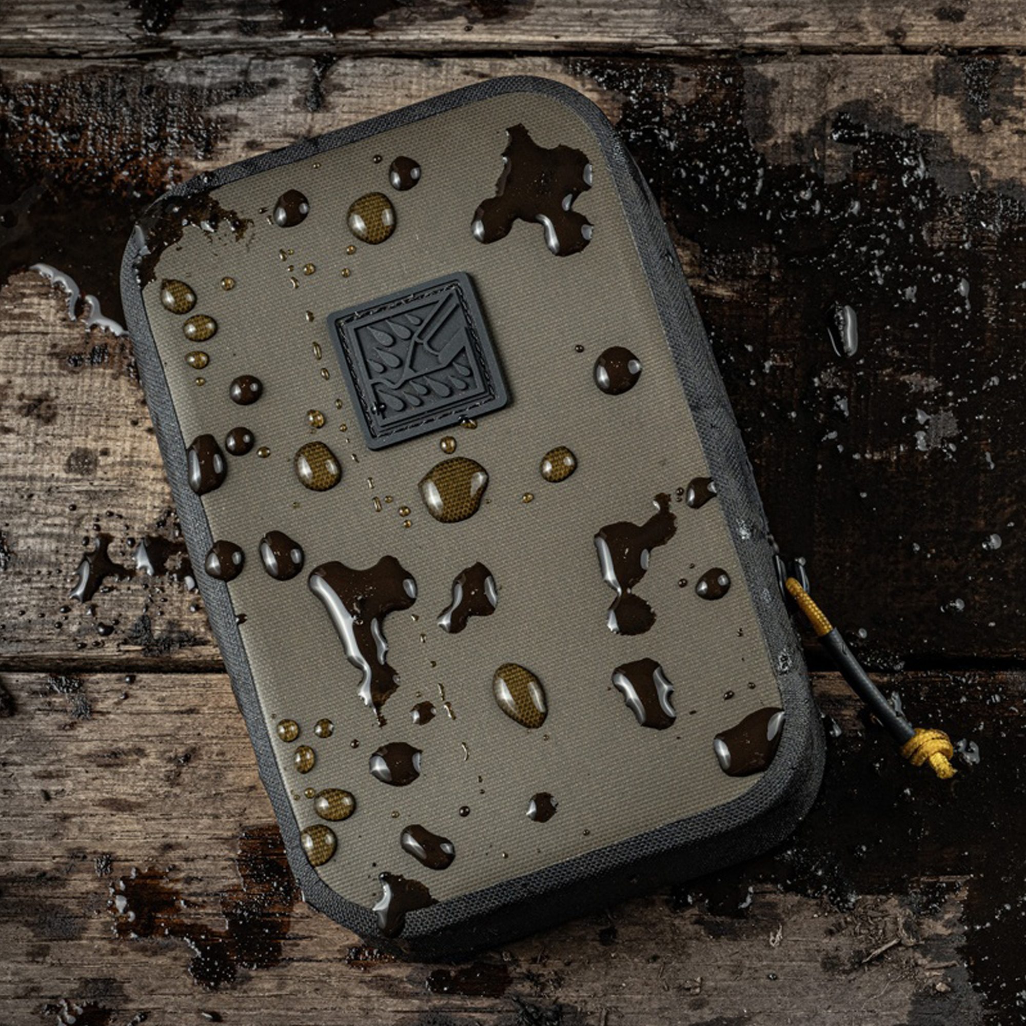 A tactical pouch shown on a dark wooden surface with water droplets on the exterior.
