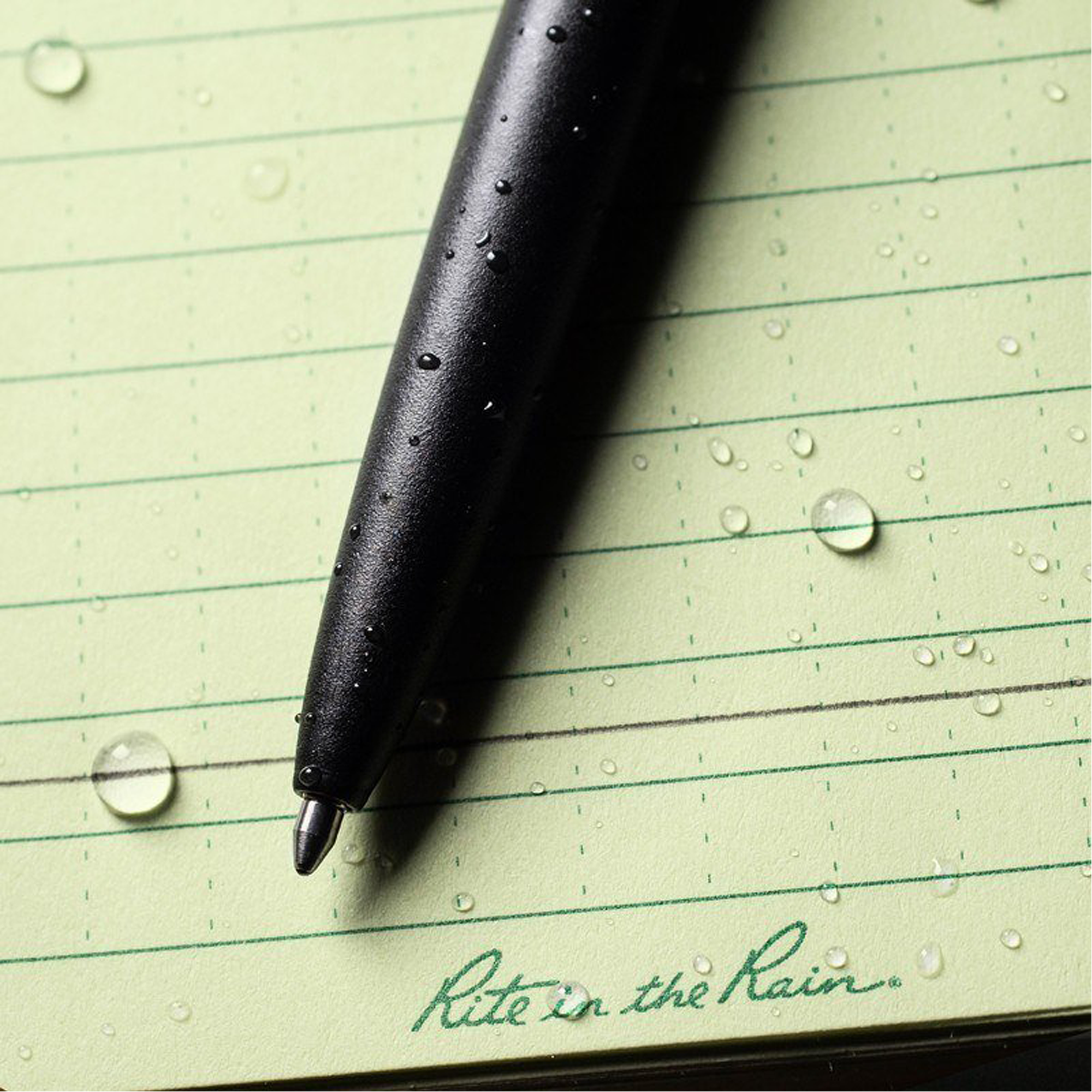 A close-up of a black pen with water droplets resting on a green paper.