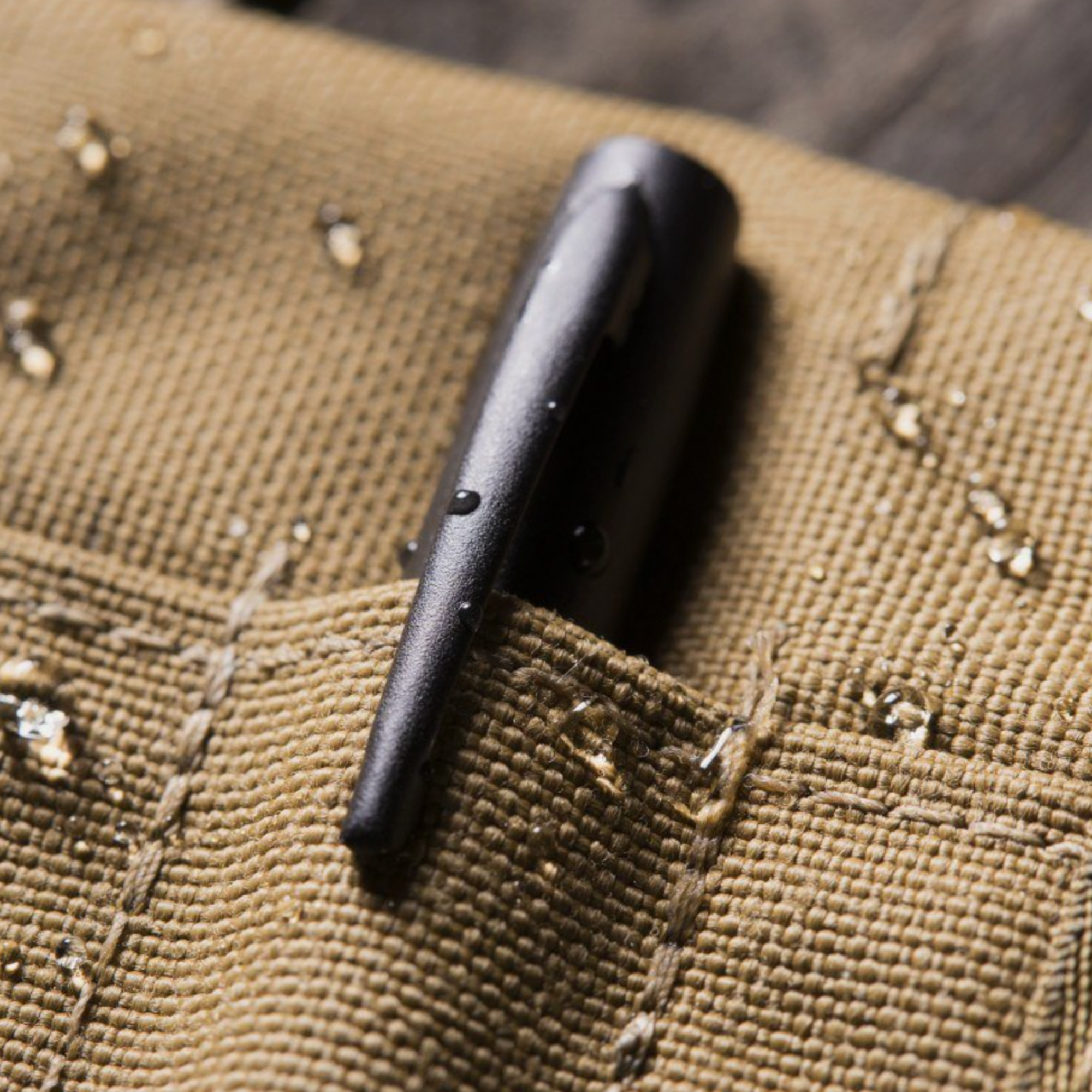 Black metal pen clip on a textured brown fabric surface