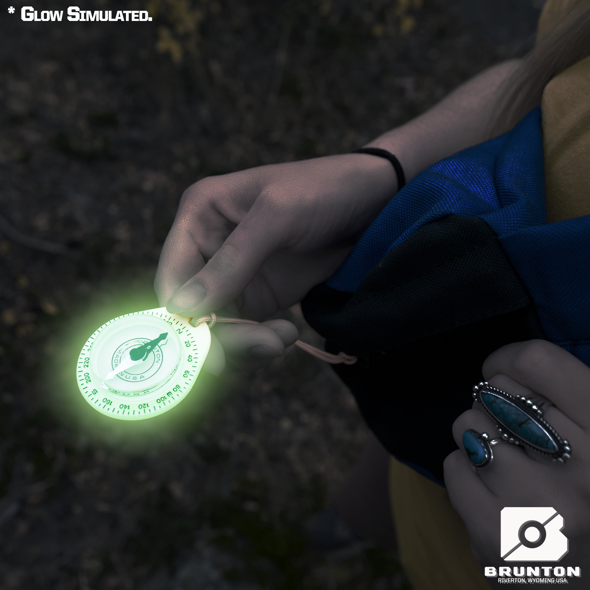 Hand holding a glowing Brunton compass against a dark background