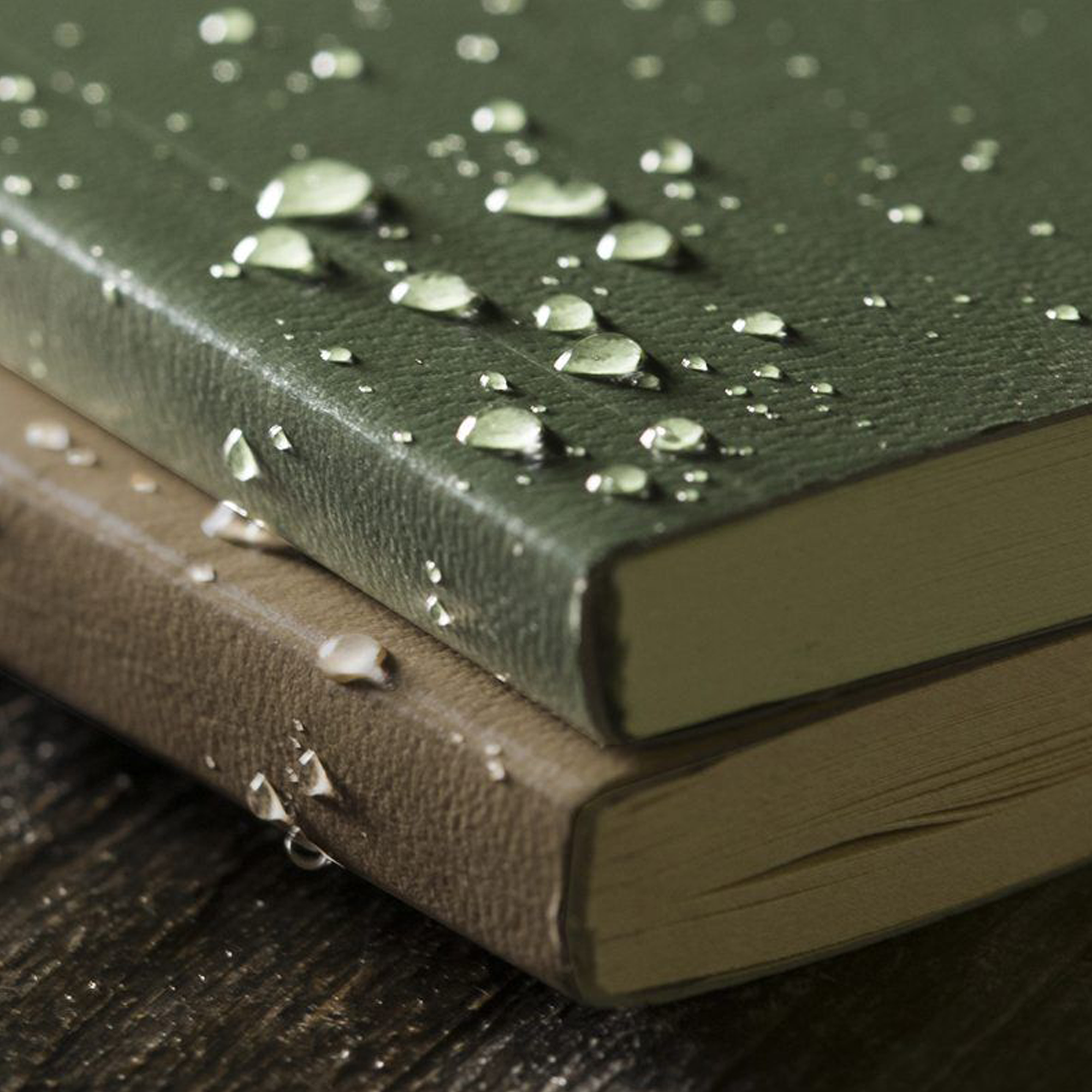 Two stacked notebooks on a dark wooden surface, with water droplets resting on the top