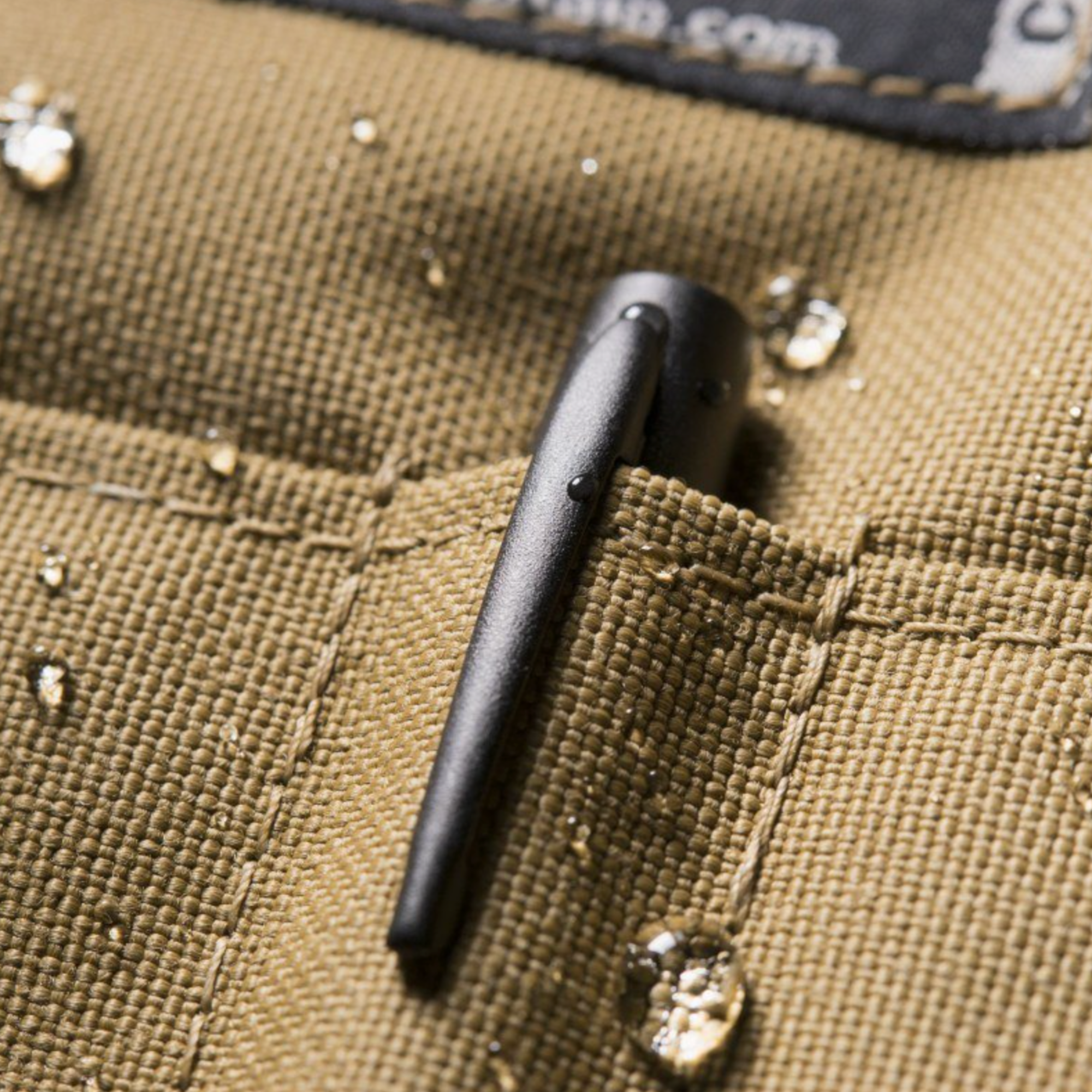 Close-up of a black metal clip on a tan fabric surface with water droplets.